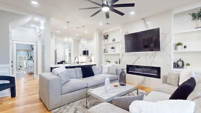 living room featuring ceiling fan, recessed lighting, a fireplace, built in features, and light wood finished floors