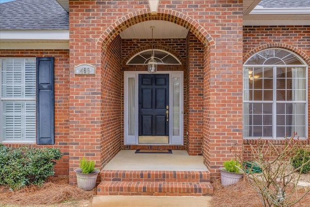 doorway to property featuring a shingled roof and brick siding