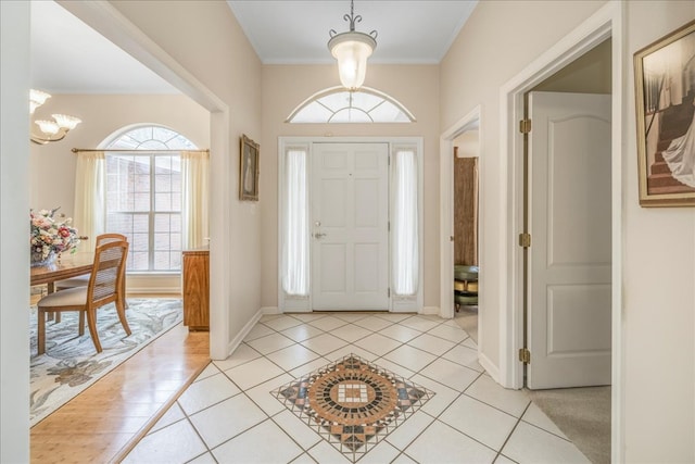 entrance foyer featuring baseboards, crown molding, an inviting chandelier, and light tile patterned floors