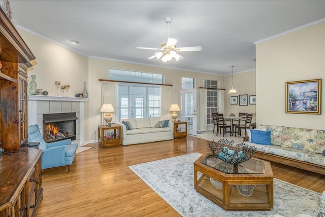 living area with a fireplace, wood finished floors, a ceiling fan, baseboards, and crown molding