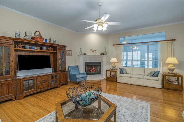 living area featuring a tiled fireplace, wood finished floors, a ceiling fan, and crown molding