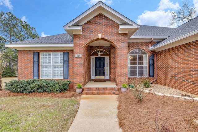 doorway to property featuring brick siding and a shingled roof