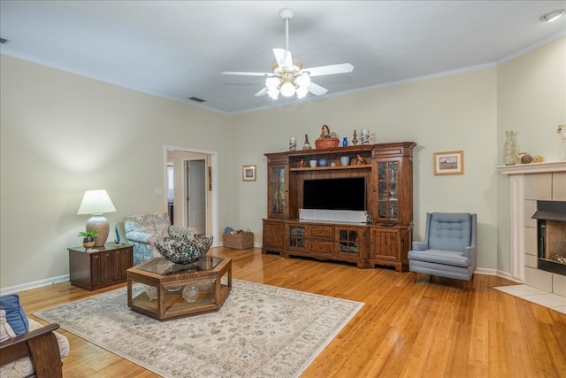 living area with crown molding, baseboards, a tiled fireplace, and wood finished floors