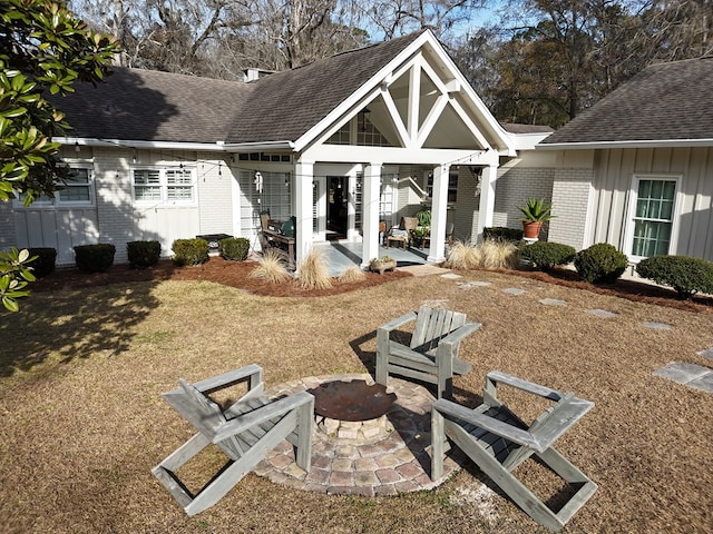 rear view of house with a patio, brick siding, roof with shingles, and an outdoor fire pit