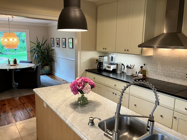 kitchen featuring crown molding, decorative light fixtures, decorative backsplash, wall chimney exhaust hood, and a sink