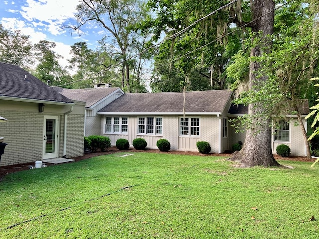 view of front of house featuring brick siding, board and batten siding, a shingled roof, and a front yard