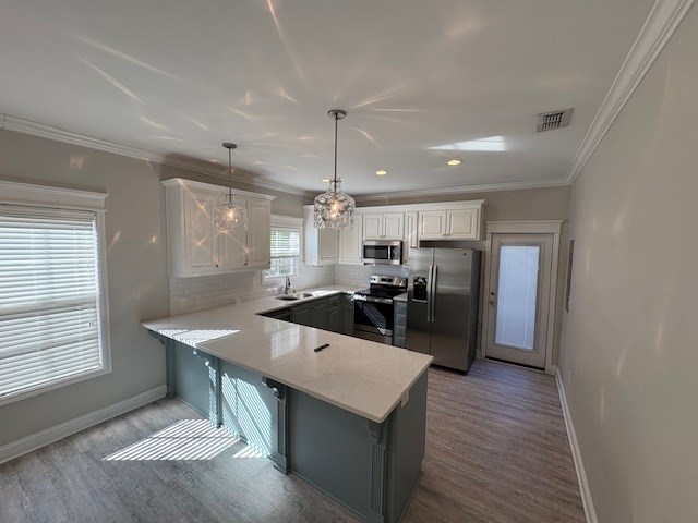 kitchen with ornamental molding, appliances with stainless steel finishes, decorative light fixtures, and white cabinets