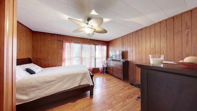 bedroom with wood walls, ceiling fan, and light hardwood / wood-style flooring