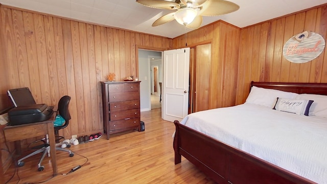 bedroom with ceiling fan, light hardwood / wood-style floors, and wood walls