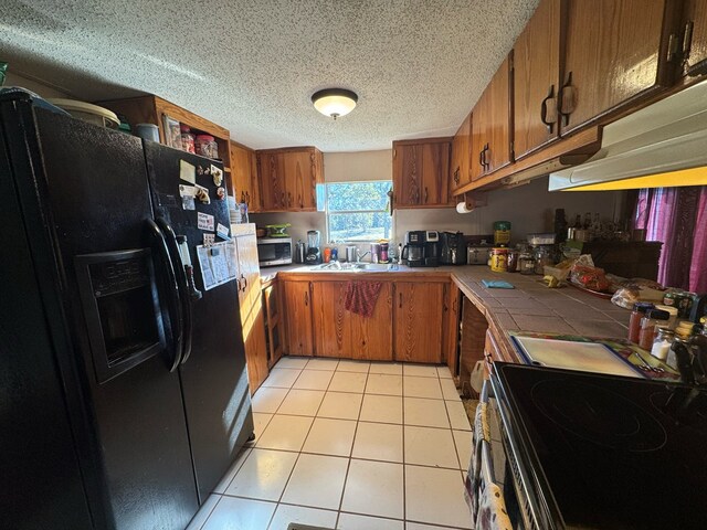 kitchen featuring light tile patterned floors, electric range oven, a textured ceiling, black fridge with ice dispenser, and tile countertops