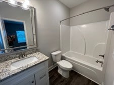 full bathroom with vanity, wood-type flooring, washtub / shower combination, and toilet