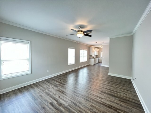 unfurnished living room with dark hardwood / wood-style flooring, ceiling fan with notable chandelier, and ornamental molding