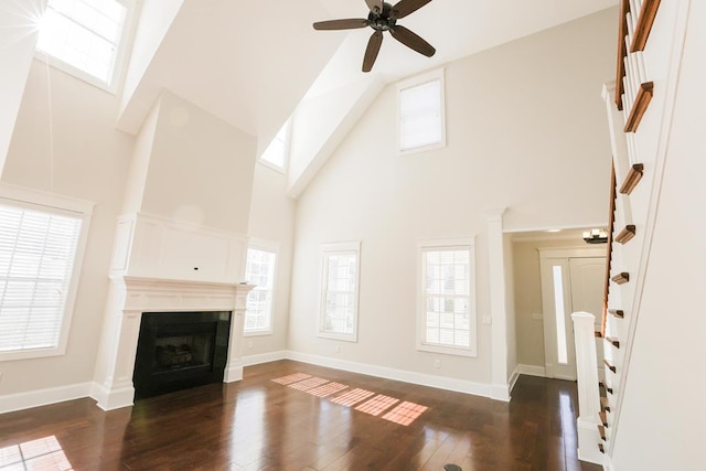 unfurnished living room with dark wood-type flooring, a wealth of natural light, high vaulted ceiling, and ceiling fan