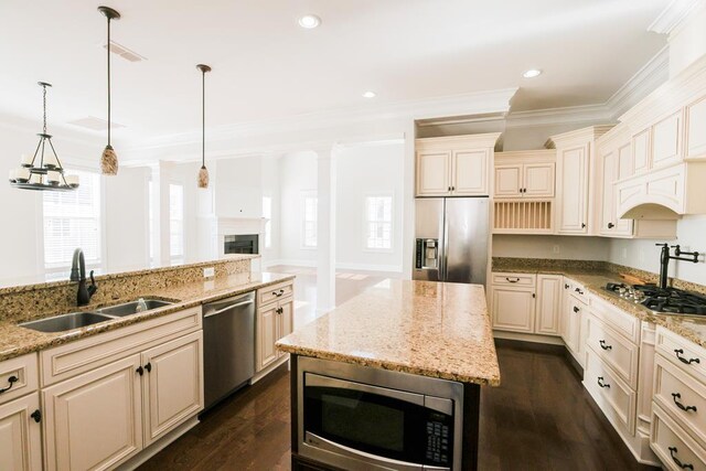 kitchen featuring appliances with stainless steel finishes, decorative light fixtures, sink, light stone counters, and cream cabinets