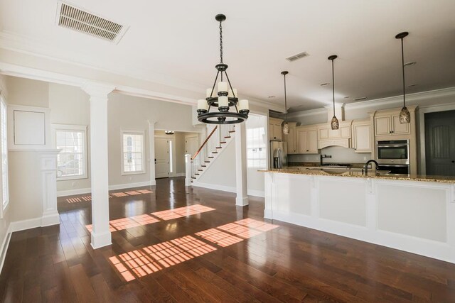 kitchen with ornate columns, hanging light fixtures, appliances with stainless steel finishes, light stone countertops, and cream cabinets