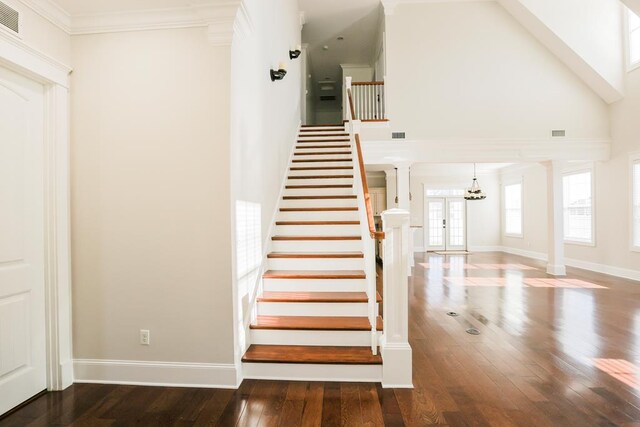 stairs with hardwood / wood-style floors, a towering ceiling, ornamental molding, and decorative columns