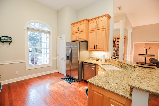 kitchen with light brown cabinetry, light wood-style flooring, appliances with stainless steel finishes, ornate columns, and a sink