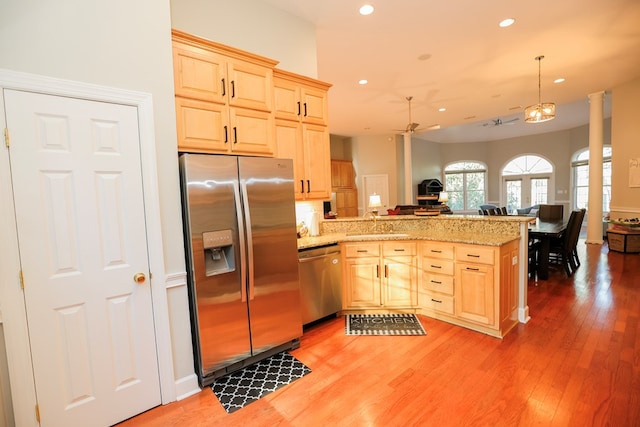 kitchen featuring stainless steel appliances, a peninsula, open floor plan, and light brown cabinetry