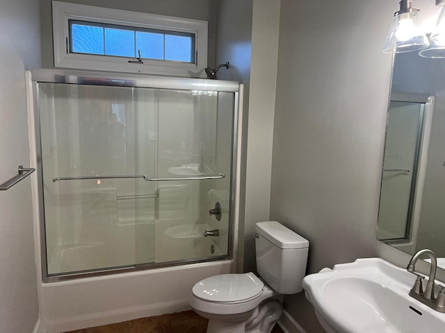 bathroom featuring toilet, combined bath / shower with glass door, and a sink