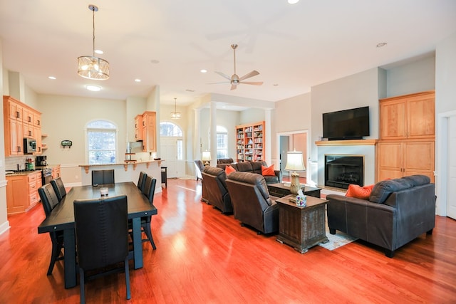 living area featuring wood finished floors, baseboards, recessed lighting, a glass covered fireplace, and ceiling fan with notable chandelier