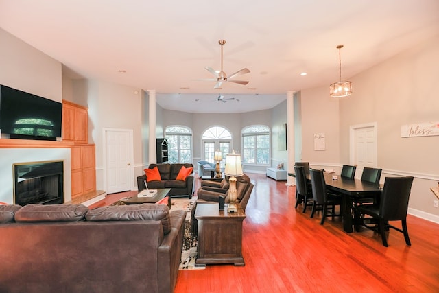 living area featuring ceiling fan with notable chandelier, wood finished floors, a fireplace with raised hearth, and baseboards