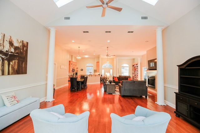 living area featuring a glass covered fireplace, decorative columns, wood finished floors, and visible vents