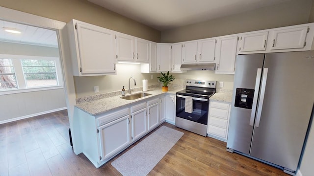 kitchen with appliances with stainless steel finishes, white cabinetry, sink, light stone countertops, and light wood-type flooring