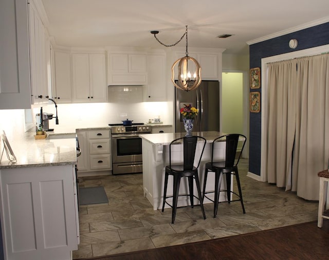 kitchen featuring a breakfast bar area, appliances with stainless steel finishes, a sink, white cabinetry, and a notable chandelier