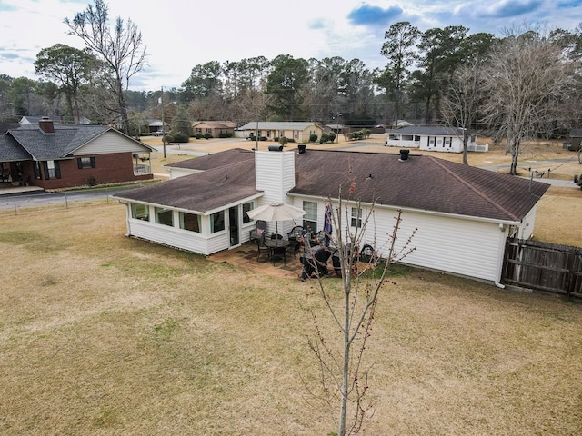 exterior space with a yard, a chimney, a shingled roof, a sunroom, and fence