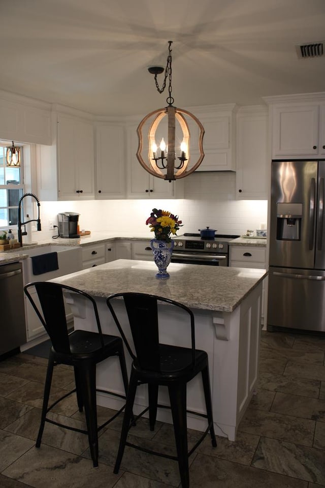 kitchen featuring decorative backsplash, appliances with stainless steel finishes, a center island, light stone countertops, and white cabinetry