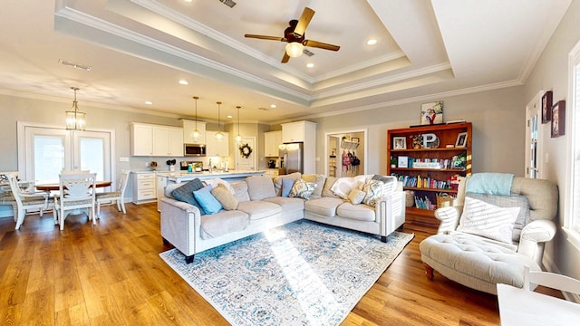 living room with recessed lighting, visible vents, ornamental molding, a tray ceiling, and light wood finished floors