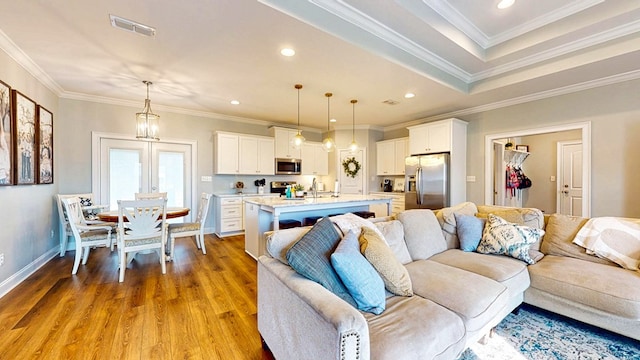 living room with light wood-type flooring, visible vents, crown molding, and recessed lighting