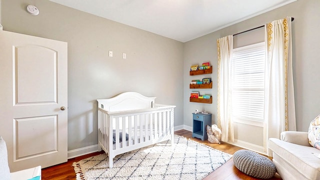 bedroom featuring a nursery area, multiple windows, wood finished floors, and baseboards