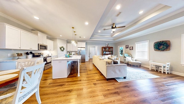 kitchen featuring light wood-style flooring, stainless steel appliances, visible vents, open floor plan, and a tray ceiling