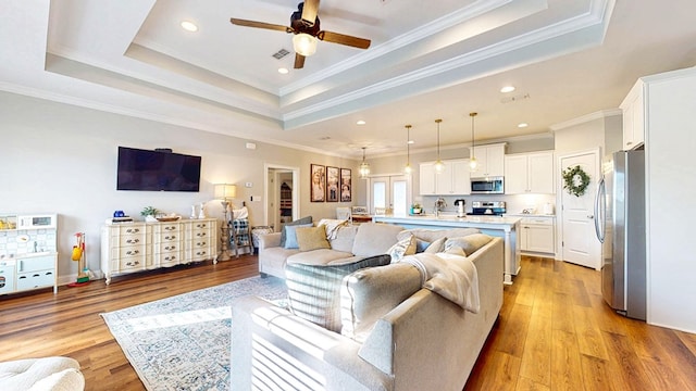 living area featuring light wood-type flooring, a tray ceiling, visible vents, and crown molding