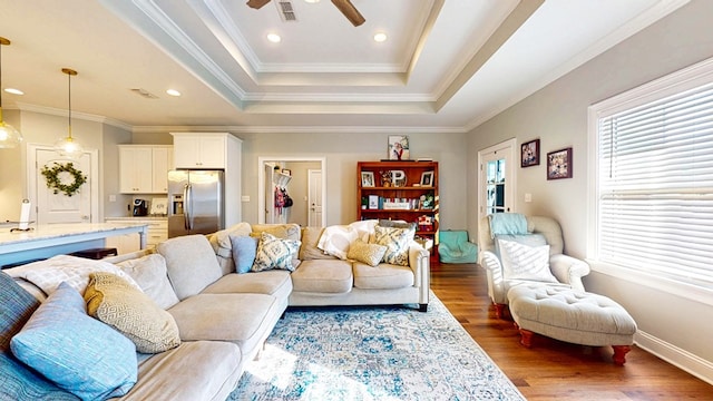 living room featuring recessed lighting, wood finished floors, visible vents, ornamental molding, and a raised ceiling