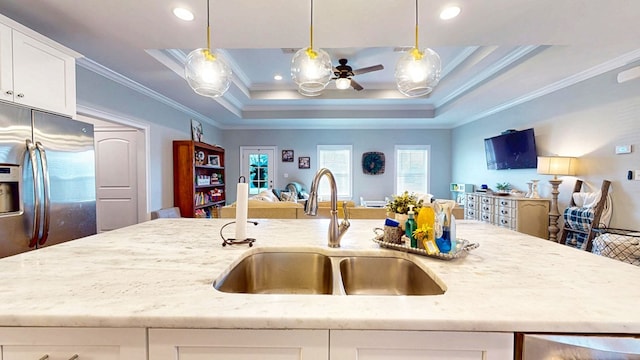 kitchen with stainless steel refrigerator with ice dispenser, a raised ceiling, open floor plan, a sink, and light stone countertops