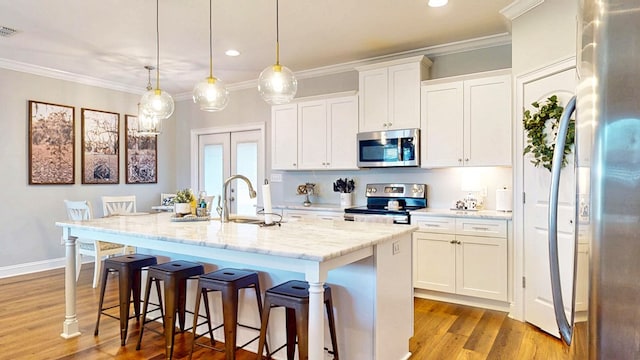 kitchen featuring appliances with stainless steel finishes, ornamental molding, a kitchen island with sink, light wood-style floors, and a sink