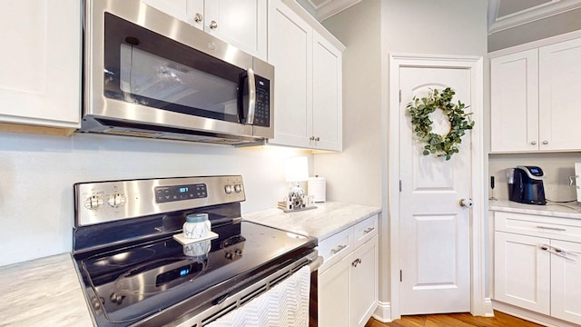 kitchen with appliances with stainless steel finishes, light wood-style flooring, light stone countertops, and white cabinets