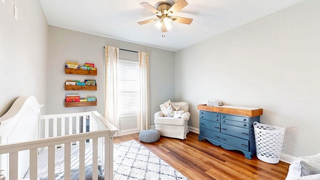 bedroom featuring baseboards, a crib, a ceiling fan, and light wood-style floors