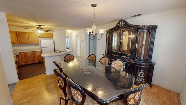 dining space featuring sink, ceiling fan with notable chandelier, and light wood-type flooring