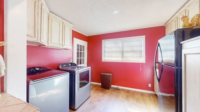 washroom with a textured ceiling, cabinets, washing machine and clothes dryer, and light hardwood / wood-style floors