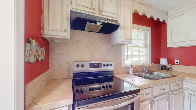 kitchen featuring stainless steel range with electric stovetop, sink, cream cabinets, and tasteful backsplash