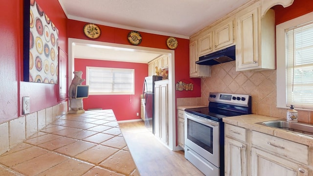 kitchen with appliances with stainless steel finishes, cream cabinetry, crown molding, tile counters, and tasteful backsplash