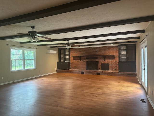 unfurnished living room with wood-type flooring, a wall unit AC, a brick fireplace, a textured ceiling, and beam ceiling