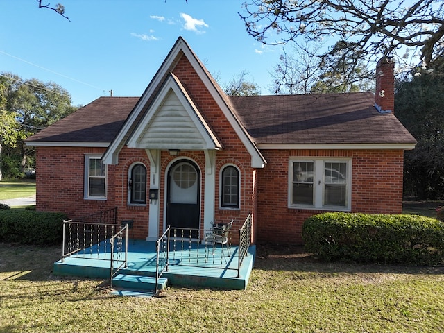 view of front facade with a shingled roof, a chimney, a front lawn, and brick siding