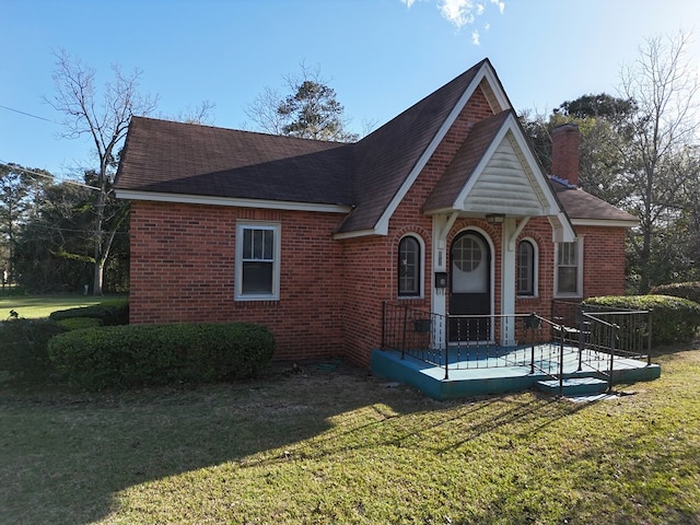 view of front of property featuring a shingled roof, a front yard, brick siding, and a chimney