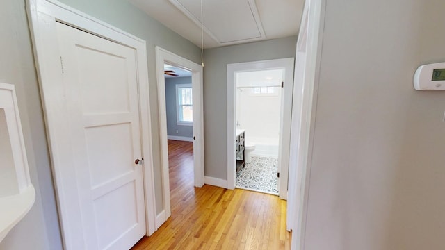 corridor featuring light wood-type flooring, attic access, and baseboards