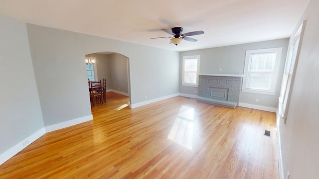 unfurnished living room with arched walkways, light wood finished floors, visible vents, a brick fireplace, and baseboards