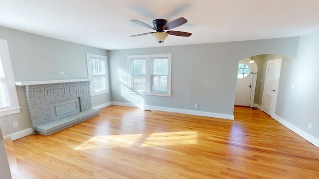 unfurnished living room with arched walkways, a brick fireplace, wood finished floors, and baseboards